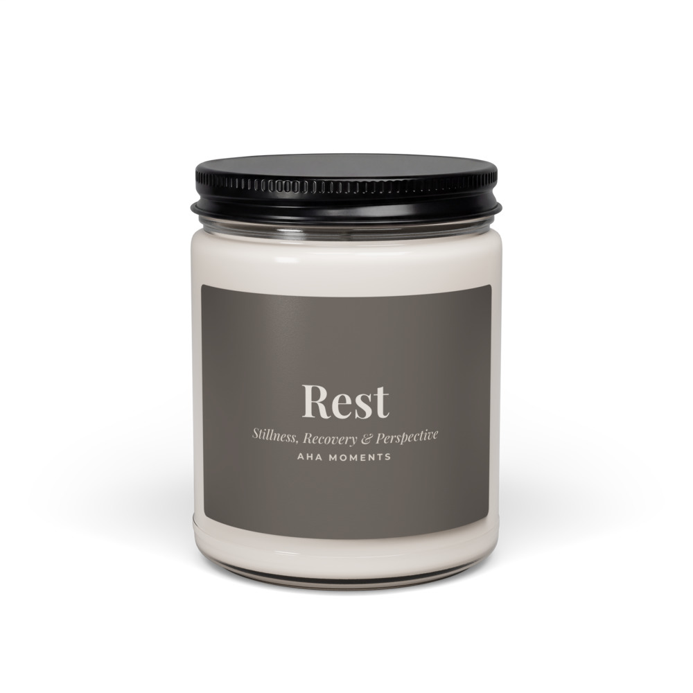 A white soy candle with a slate label that reads Rest, Stillness, Recovery and Perspective, Aha Moments.