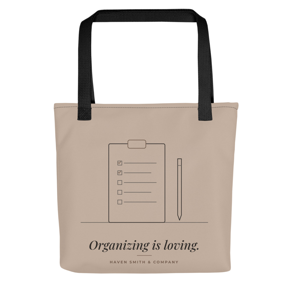 A sand tote with black handles printed with a clipboard drawing and Organizing is loving.