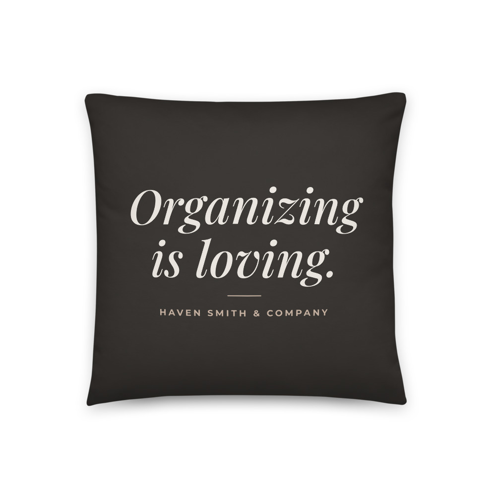 A charcoal square pillow printed with Organizing is loving and Haven Smith and Company in cream.